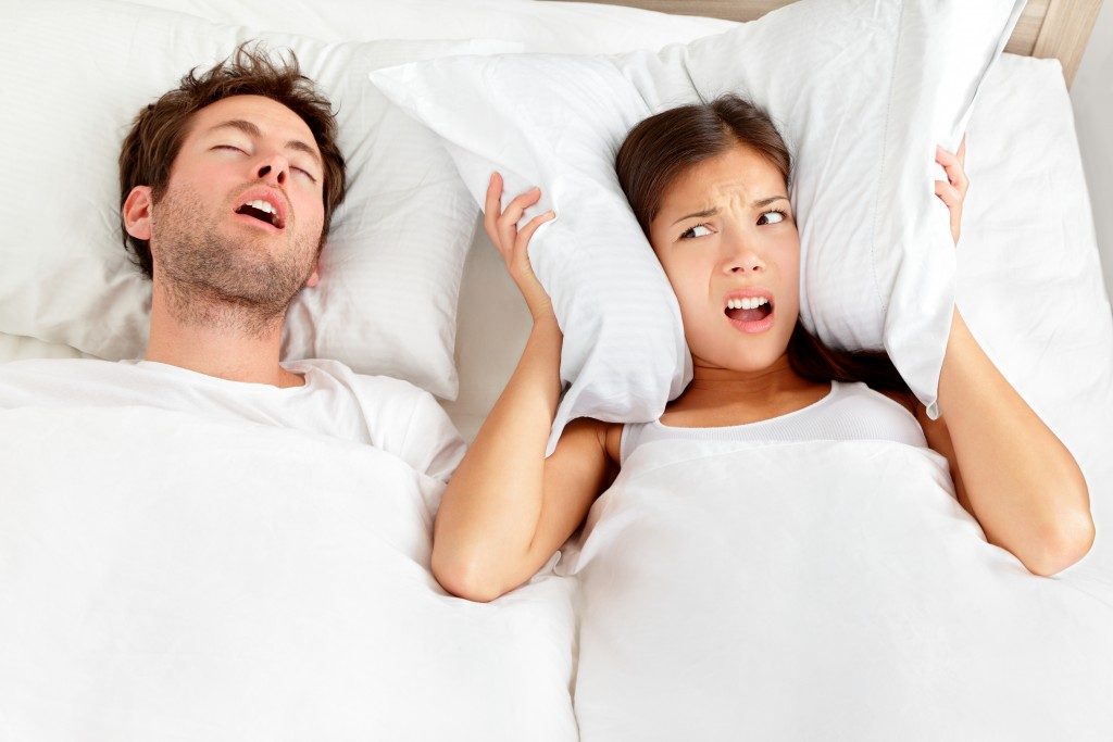 man snoring and woman can not sleep, covering ears with pillow