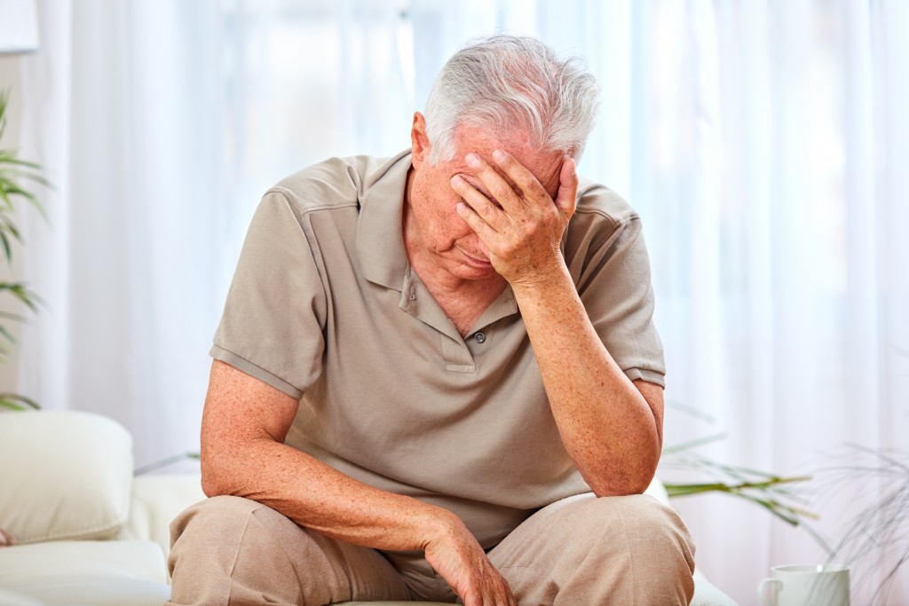 elderly man sitting and covering his face, not feeling good