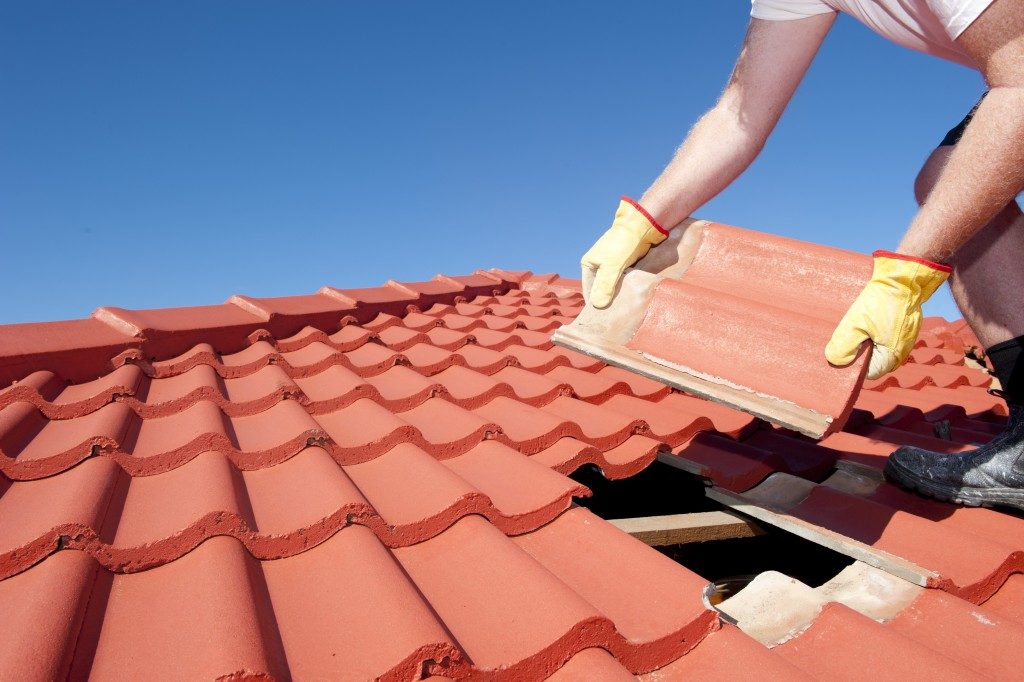 worker with yellow gloves replacing red tiles or shingles on house with blue sky as background