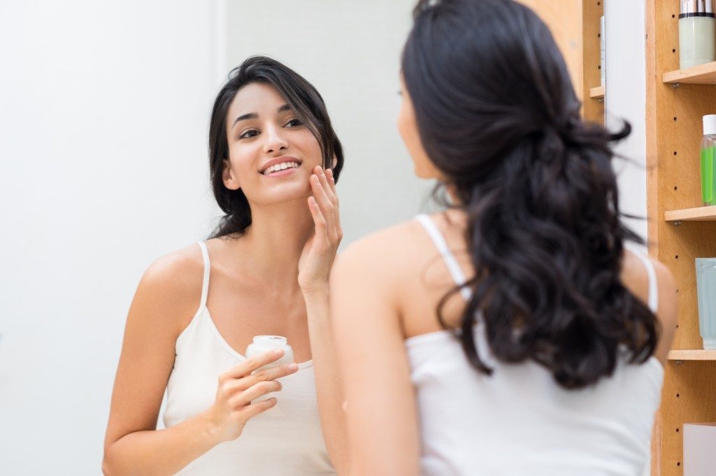 Woman caring of her beautiful skin on the face standing near mirror in the bathroom