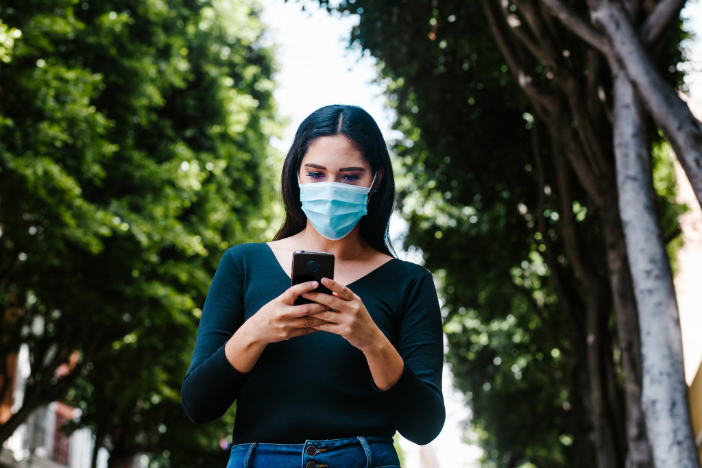 woman wearing face mask while using her smartphone traveling outside her house