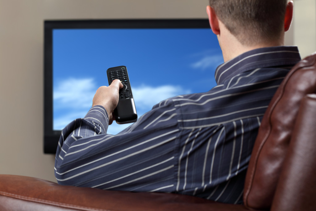 man on a brown leather chair pointing his remote on a tv