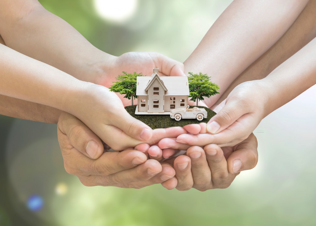 Safe family home model and garden on son daughter children kid guardian mother father hands, blur natural greenery tree planting environment background: Home loan property ownership assurance concept