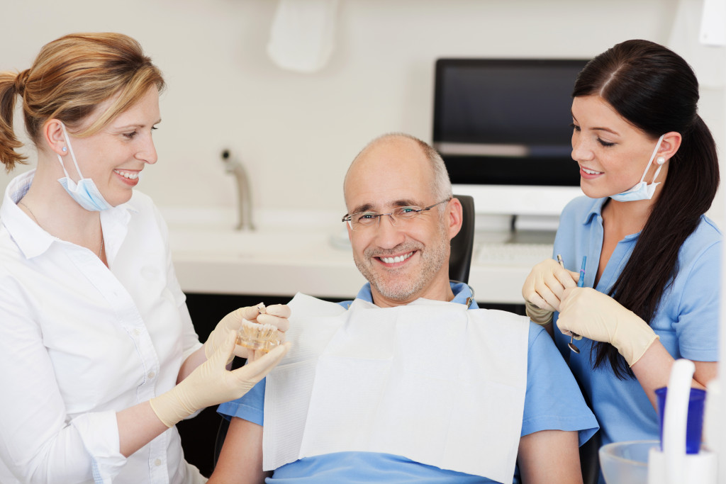 dentist with her assistant treating an old man