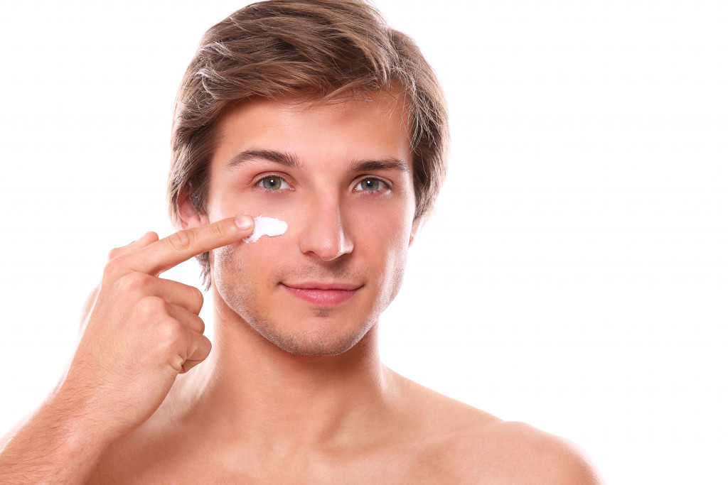 handsome man is smiling while applying cream on his face