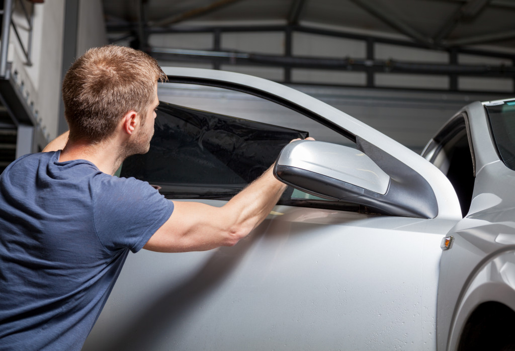 A man applying tinting foil on a car window in a garage