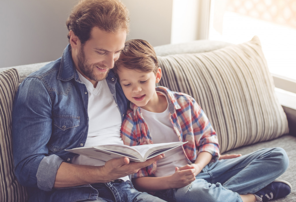 a father reading a book to his son while on a couch
