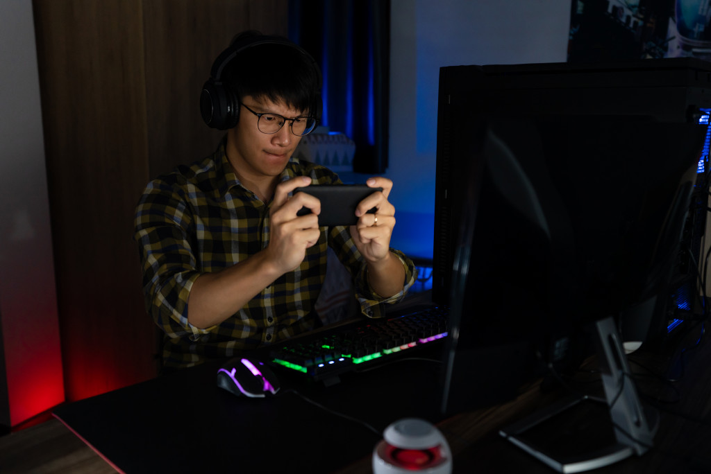 a man playing games using a phone in front of a PC in a man cave