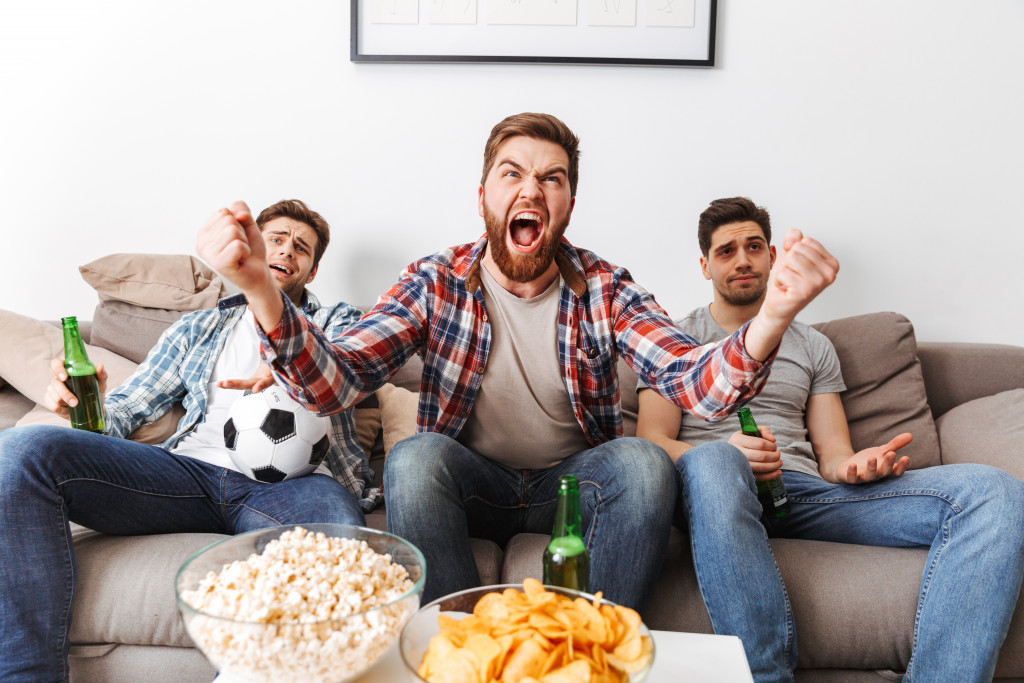 3 men watching tv game with beers and popcorn