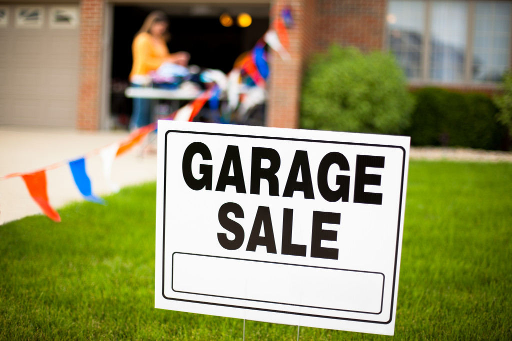 Garage sale sign in front of a yard with a woman organizing items on a table