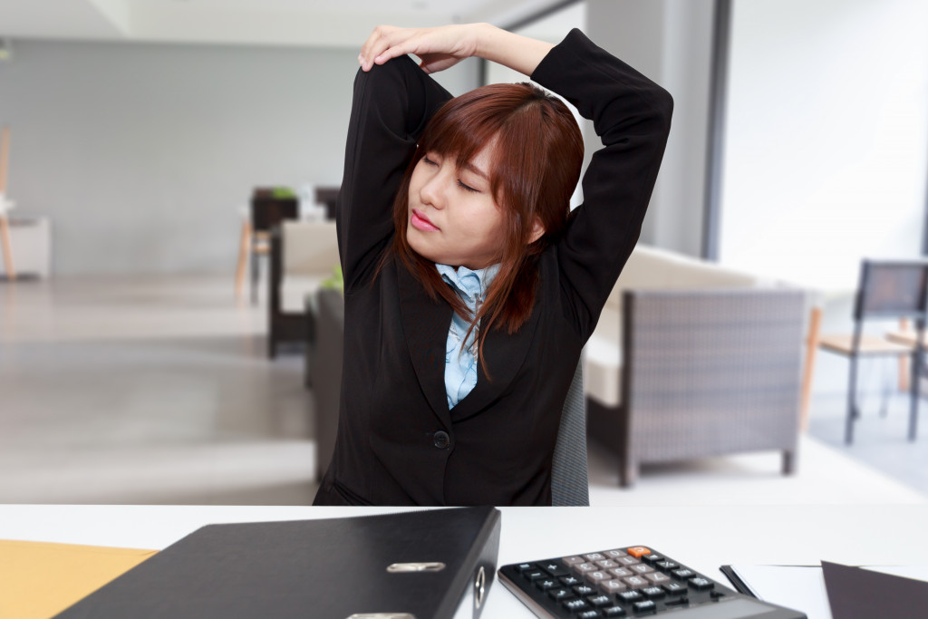 Businesswoman performing stretching exercises while working at her desk.