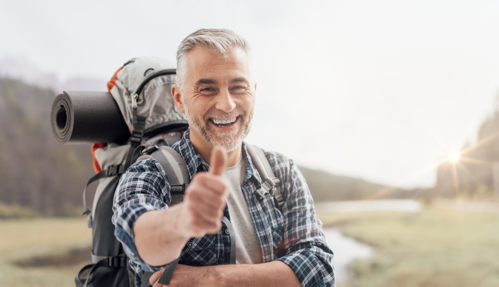 Senior man carrying hiking backpack smiling after retirement 