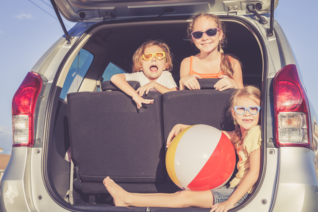 Happy sisters and a brother in the back of a car as they prepare for a family road trip.