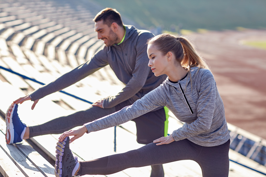 A man and woman wearing sportswear while stretching their legs