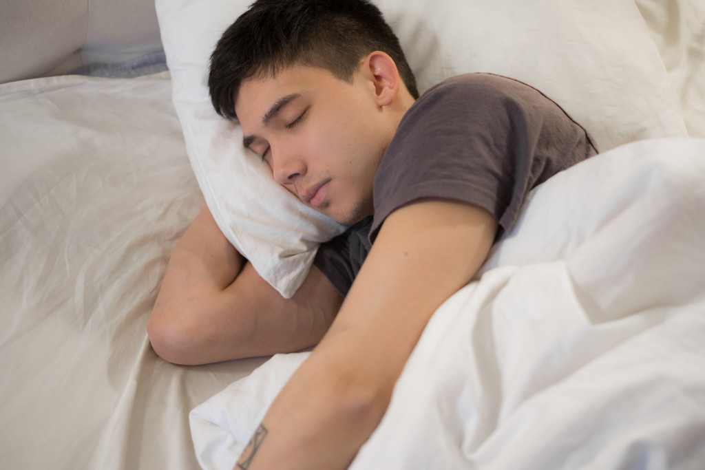 a man in a grey shirt sleeping peacefully in bed