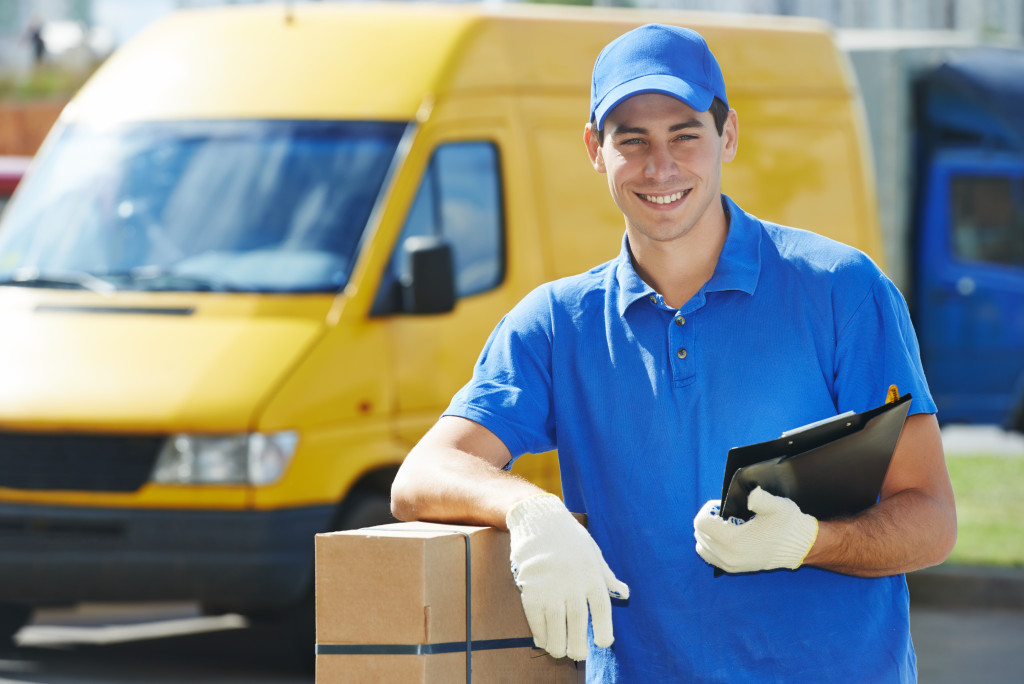 A man in a uniform holding a clipboard and a package in front of his delivery van